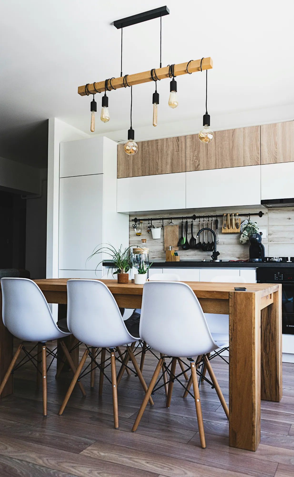 Kitchen and dining area with a solid wood table, white chairs and hanging bulb lights